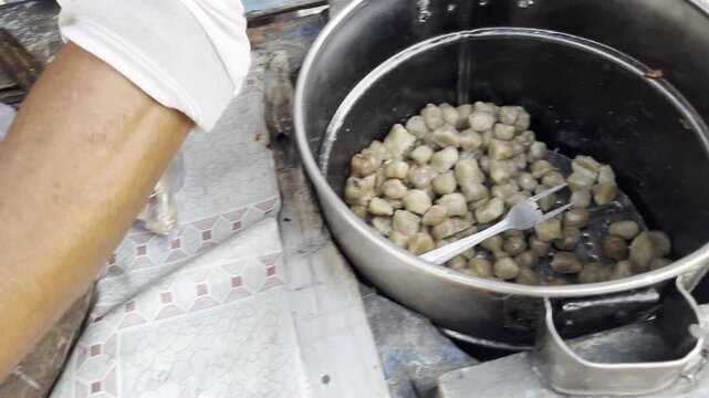 Indonesian street food vendor serving hot siomay pentol dumplings into plastic bag