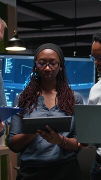 Vertical screen view of portrait of engineering team developing AI algorithms in high rise office. Teamworking colleagues debug 3D neural network brain models shown on screen.