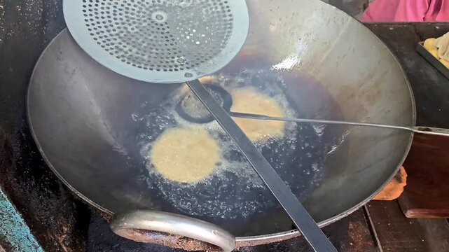 Indian street food vendor deep frying fresh puris in a large wok with boiling hot oil