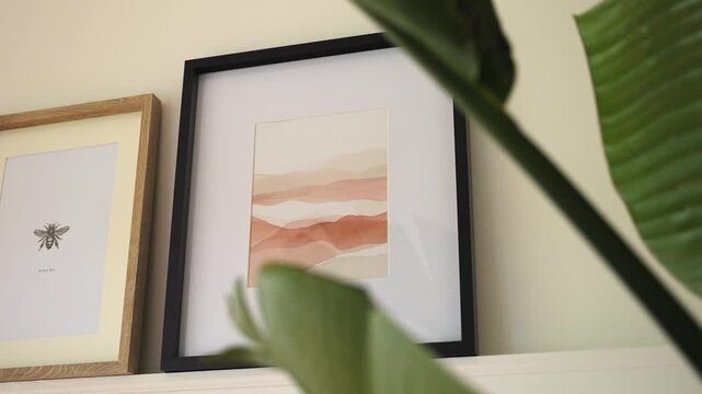 Two framed pictures on a shelf with a plant nearby indoors