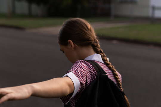 girl wearing a school dress and backpack walking and balancing on a suburban street