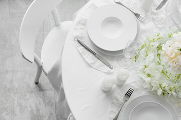 Obraz premium Elegant white table setting with dinnerware, cutlery, candles, and floral decor for special occasions