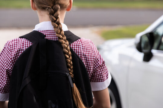 school girl walking to the car wearing uniform and with a backpack on