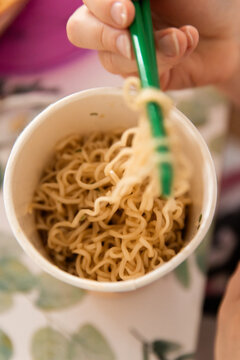 instant noodles in a cup being eaten using green chopsticks