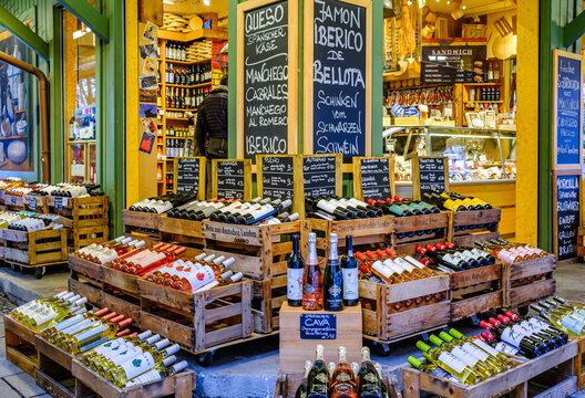 Wine bottles arranged in wooden crates outside a shop during daylight in a lively market area, inviting passersby to explore various selections