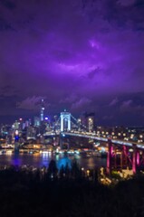Obraz premium Night city skyline with glowing bridge lights and purple dark sky over the water reflection in the harbor
