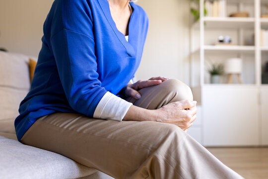 Senior woman experiencing knee pain while sitting on sofa at home
