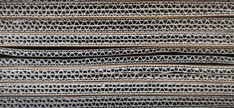 Close-up texture of stacked corrugated cardboard sheets, brown paper pattern background.