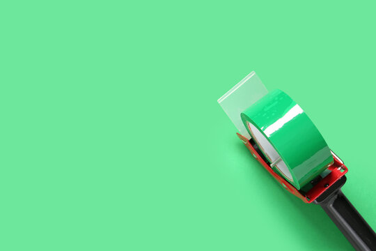 Green packaging tape dispenser with clear plastic blade on solid mint background for shipping and office supplies, this essential office and shipping supply is ready for sealing boxes and parcels