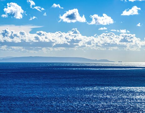 Serene ocean scene under a bright sky with puffy clouds. A distant island silhouette