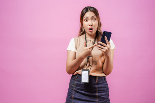 Shocked young Asian woman is pointing to her smartphone with a surprised expression on her face.