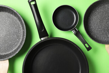 Assorted non-stick frying pans and skillets for home cooking and kitchenware, top view on green...