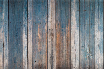 Fototapeta premium Weathered vertical wooden planks painted in faded blue and natural brown tones create a rustic textured background.