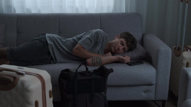 Relocation fatigue and homesickness. Young man lying on bed in temporary apartment feeling emotionally exhausted after moving