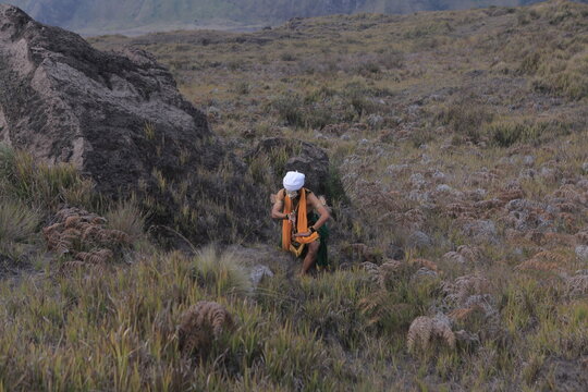 Traditional Javanese mask dancer performing outdoors amidst large volcanic rocks and mountains.