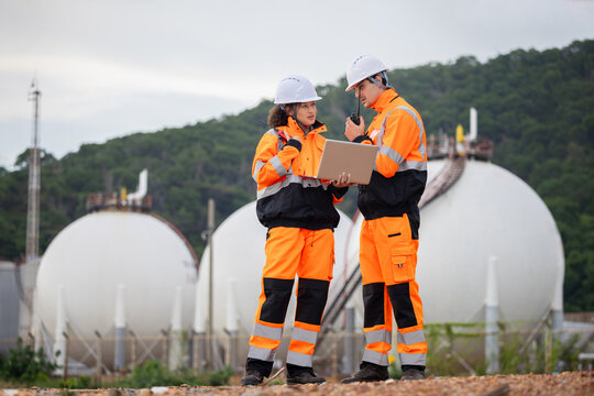 Team of technical in safety uniform discussing maintenance plan at fuel storage facility, Industrial engineer and worker using laptop and radio to monitor gas storage tank system