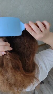 Woman braiding her own long brown wavy hair into a French braid or fishtail plait at home. Close-up over-the-shoulder rear view. Morning beauty routine, hair care, and styling concept video.