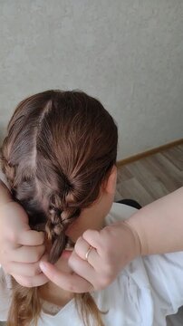 Woman braiding her own long brown wavy hair into a French braid or fishtail plait at home. Close-up over-the-shoulder rear view. Morning beauty routine, hair care, and styling concept video.