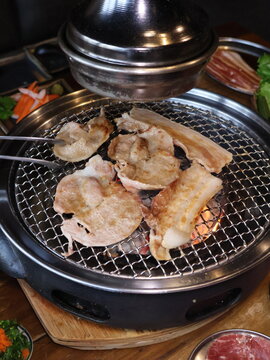 Grilled pork sizzling over a charcoal barbecue.