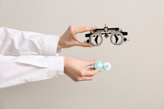 Doctor hands with optical trial frame and container of contact lenses on white background