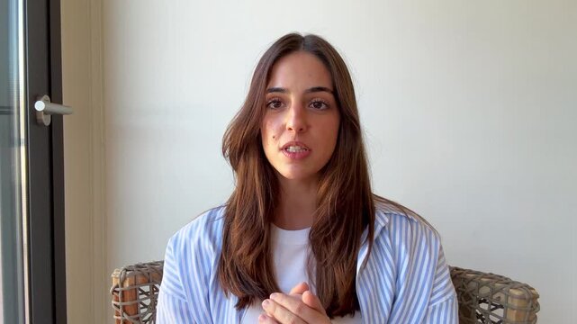 Confident young businesswoman speaking and gesturing during an online video conference call, explaining a project or giving a presentation while working remotely from her home office
