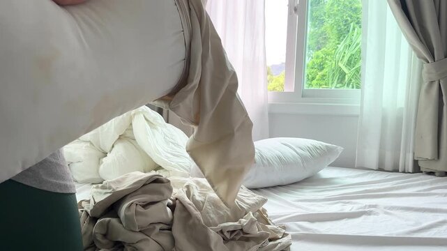 Home video footage of a woman putting clean bed linen on a bed in a bright bedroom, changing sheets as part of a daily housekeeping routine.