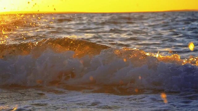 Cinematic close up of ocean wave crashing with splashing water droplets during golden hour sunset.