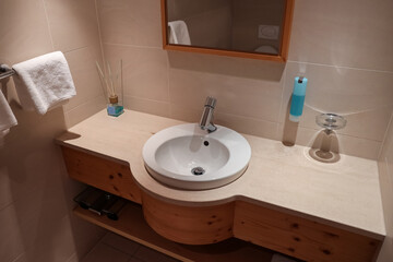 Fototapeta premium Modern bathroom vanity with white sink, chrome faucet, wooden cabinetry, and beige tiled walls for home interior design
