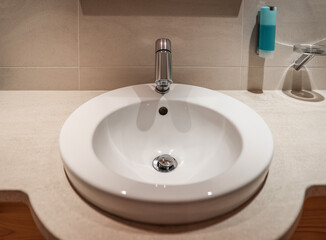 Fototapeta premium Modern bathroom sink with chrome faucet and soap dispenser, clean hygiene and sanitation concept, the clean countertop and tiled wall emphasize hygiene and sanitation in a contemporary interior