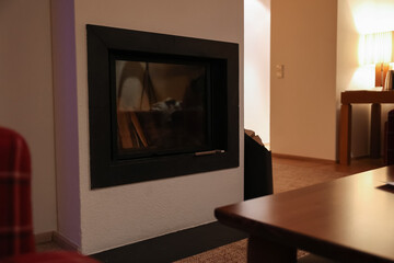 Obraz premium Modern fireplace with glass screen and wood logs in a cozy living room interior, warm home ambiance