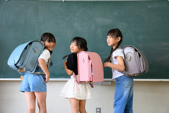教室の黒板の前でカラフルなランドセルを背負い笑顔で振り返る新入生の女の子たち