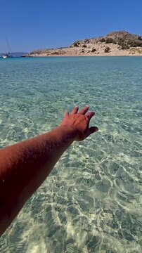 Experience the crystal-clear waters of Simos Beach on Elafonisos Island. This paradise invites you to immerse your hand in the gentle waves, showcasing the beauty of Greeces coastline.