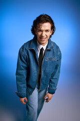 Fototapeta premium Emotional young man expresses joy in stylish denim attire against a blue backdrop
