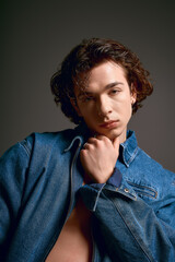 Obraz premium Young man with curly hair and stylish denim attire showcasing emotional depth in a studio setting