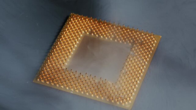 Computer CPU processor with gold pins rests on a dark surface as thick white smoke dissipates. Dramatic close-up shot highlights the intricate pin grid array and the swirling vapor effect.