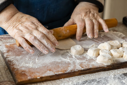 Elderly hands use a wooden rolling pin to flatten dough on a floured surface, preserving the authentic traditions of homemade dumpling preparation within a warm, cozy home kitchen