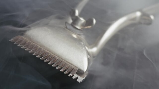 Vintage manual hair clipper rests on a dark surface, shrouded in thick white smoke. Camera pulls back in slow motion, revealing the antique tool as dramatic vapor swirls and dissipates.