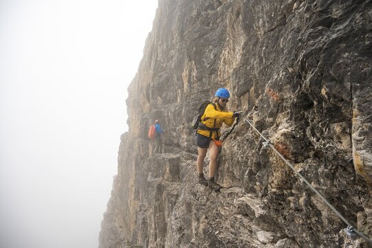 Mountaineers on a ladder on the Via Ferrata Oliva Detassis via ferrata in fog, rocky mountain peaks and mountain landscape, Brenta Mountains, Parco Naturale Brenta-Adamello, Trentino, Italy
