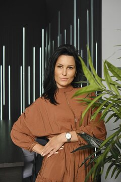 Casual lifestyle portrait of charming woman with black hair wearing brown dress posing near the potted plant
