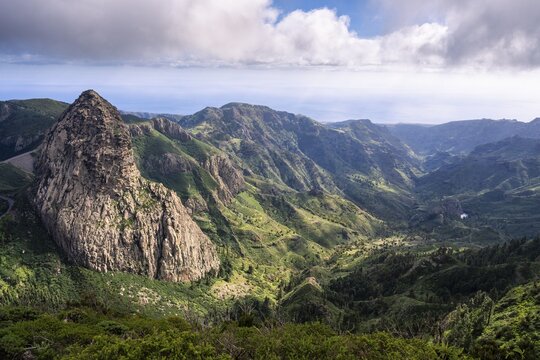 View of the Roque de Agando rock tower from the Mirador del Morro de Agando. To the right is the Barranco de Benchijigua gorge. During the day, sun and clouds, good weather. Monumento Natural de Los Roques, Reserva Natural Integral Benchijigua, La Gomera, Canary Islands, Spain