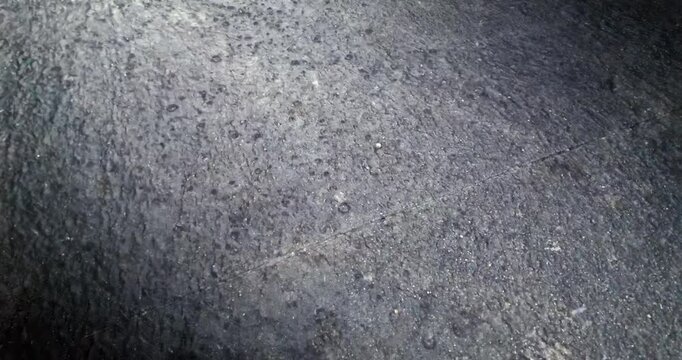 Slow motion close up: heavy rain strikes a dark, wet asphalt surface, creating scattered ripples.

