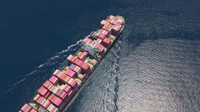 Aerial view of a large container ship moving at full speed across the open ocean, with its deck fully loaded with colorful intermodal containers ready for international trade and delivery