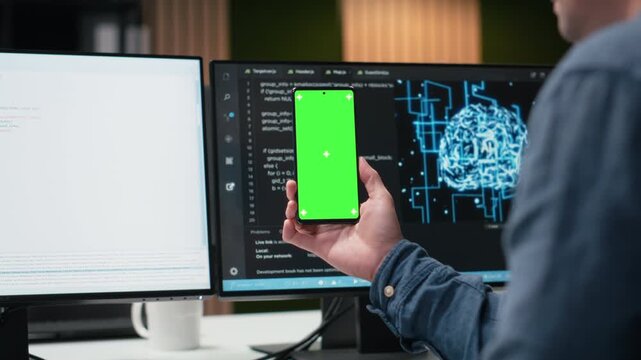 Green screen smartphone used by programmer in tech startup office developing apps. IT specialist creating applications for chroma key mobile phone, debugging glitches, close up for coding workflows.