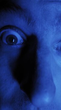 Extreme close up shows male eyes widening and looking around frantically. Saturated blue lighting creates a paranoid and surreal sci-fi atmosphere.