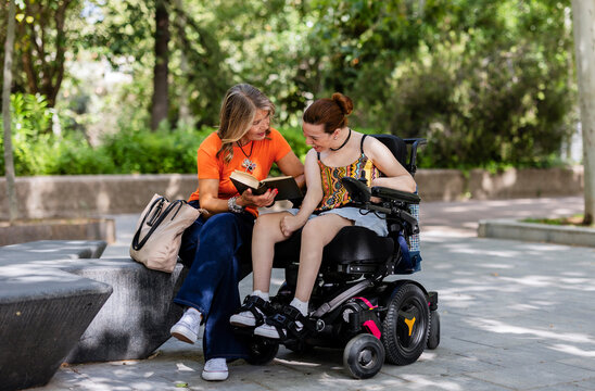 Woman reading book to young woman in wheelchair