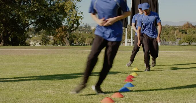 Stepping male teammates in blue shirts performing lateral cone drill on field with cones