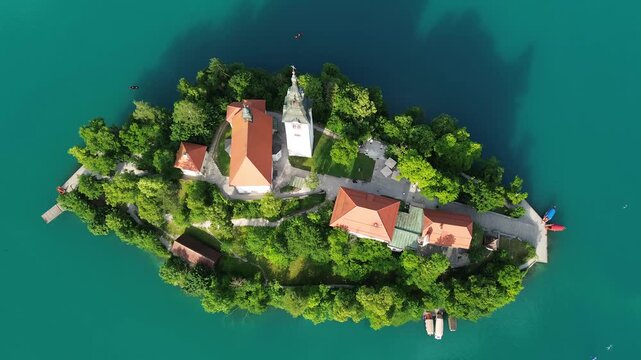 Top-down aerial view of Bled Island and the Assumption of Mary Church on Lake Bled, Slovenia. Cinematic drone footage of the historic island surrounded by vibrant turquoise water in summer.