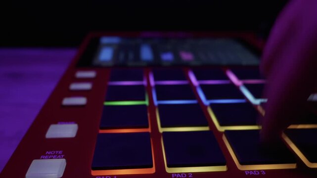 A musician creates a beat by tapping on the colorful LED pads of a midi controller. Concept of electronic music production, creative studio workflow, and modern audio technology.