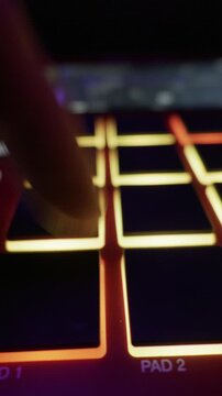 Close up of beatmaker hands playing rhythms on illuminated sampler pads with smooth slider movement. Concept of music production, nightlife creativity, and electronic sound engineering.