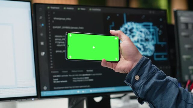 Green screen mockup smartphone used by IT specialist developing AI algorithms in high rise office. Admin taking break from debugging neural network models to use chroma key mobile phone.